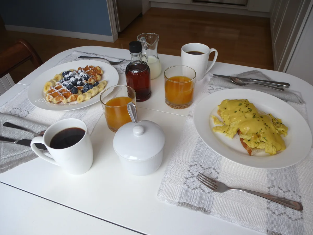 The breakfast table set with waffles, scrambled eggs, coffee and juice